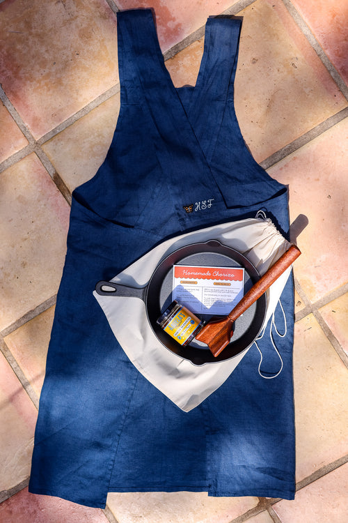 Abuela's Homemade Chorizo Kit laid out on a blue linen apron: cast iron skillet, Original chorizo seasoning, teak chopper and dust bag