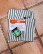 Folded Green Stripe linen apron with the recipe card and a jar of Verde chorizo seasoning on terracotta tile