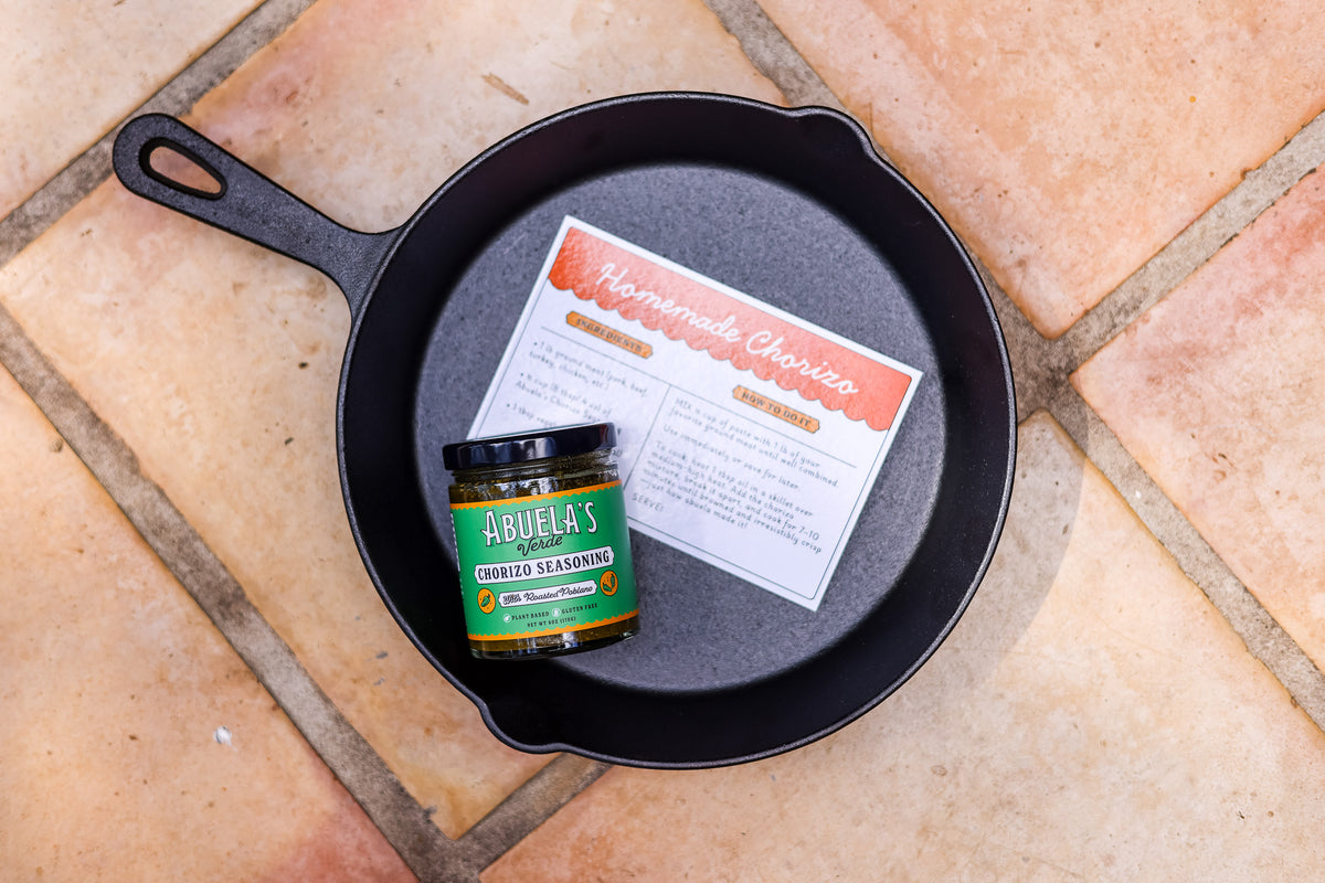 Cast iron skillet on terracotta tile with the recipe card and a jar of Verde chorizo seasoning