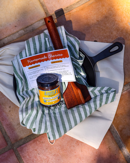 Chorizo kit gift bundle with the Green Stripe apron tucked in the skillet, Original seasoning jar and teak chopper