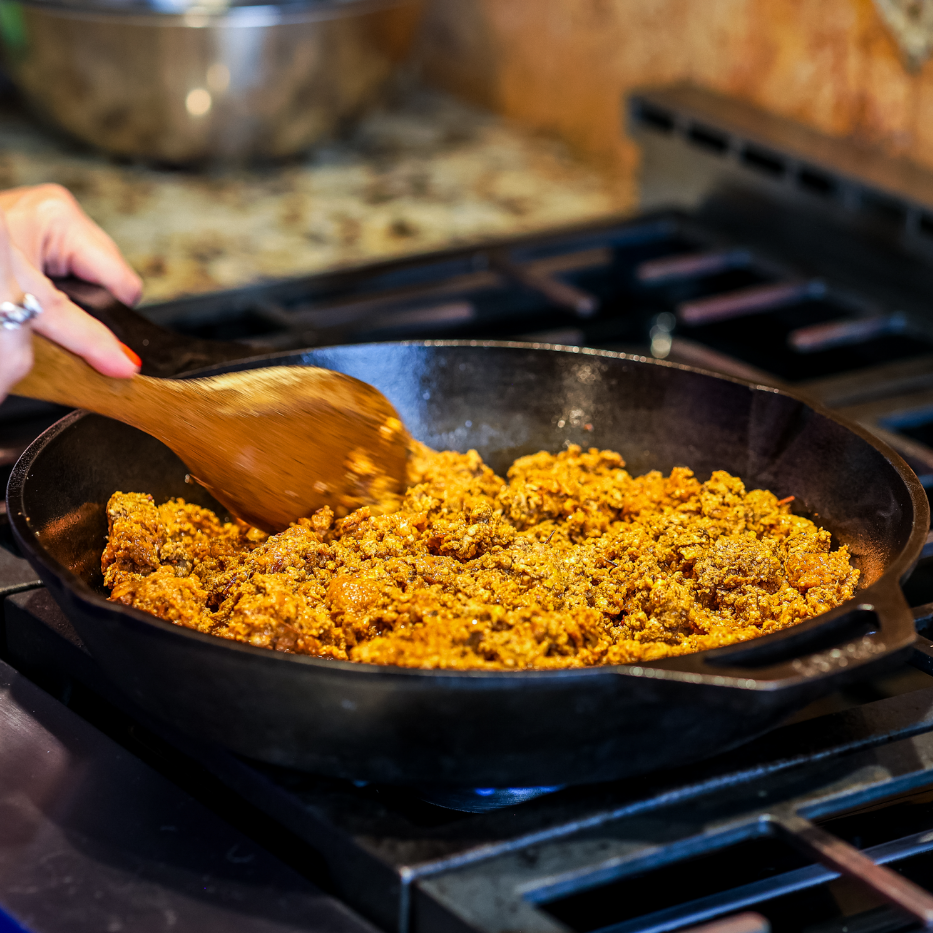 Cooking ground meat in a skillet on a stove with a wooden spoon.